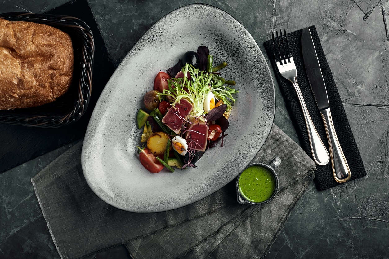 Vegetable salad with fresh tuna and avocado citrus in a gray plate on a gray slate, stone or concrete background. Top view with copy space